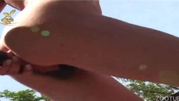 Fair-complexioned dark-haired woman in black outfit performing fellatio on a horse's penis outside