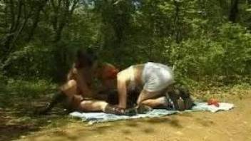 Two matures are enjoying oral sex in the forest with a black dog